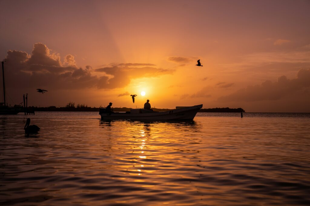 Sunset view of fisherman on the sea with birds flying over.