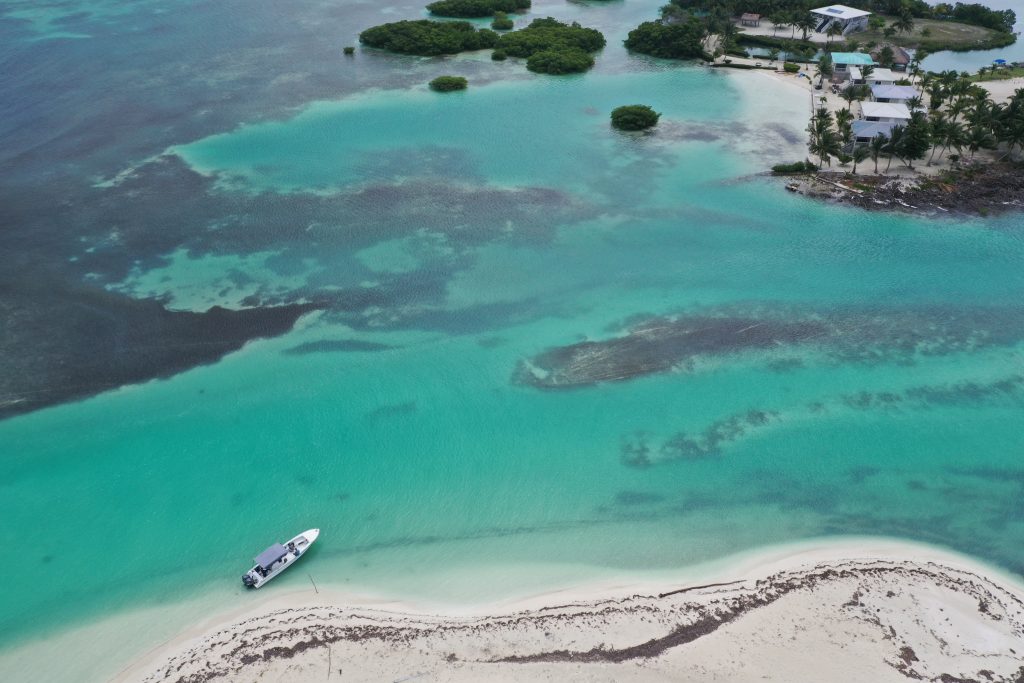 aerial photo of belize white sand beach contrasting against blue waters and boat in the water